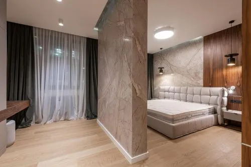 Modern bedroom with light wood flooring, a large bed with tufted headboard, marble accent walls, and sheer white curtains over a window.