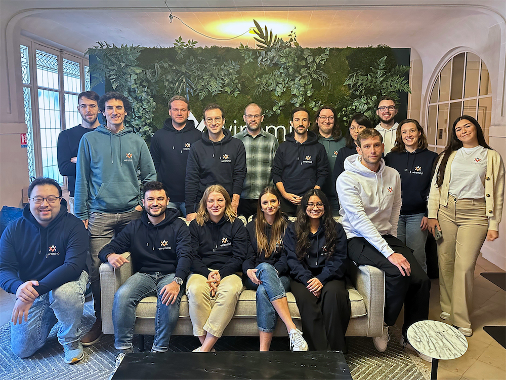 Groupe de 16 personnes posant ensemble dans un bureau avec un mur végétal en arrière-plan et plusieurs portant des sweatshirts avec le logo Wiremind.