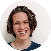 Young person with medium-length brown hair smiling broadly against a plain light background.