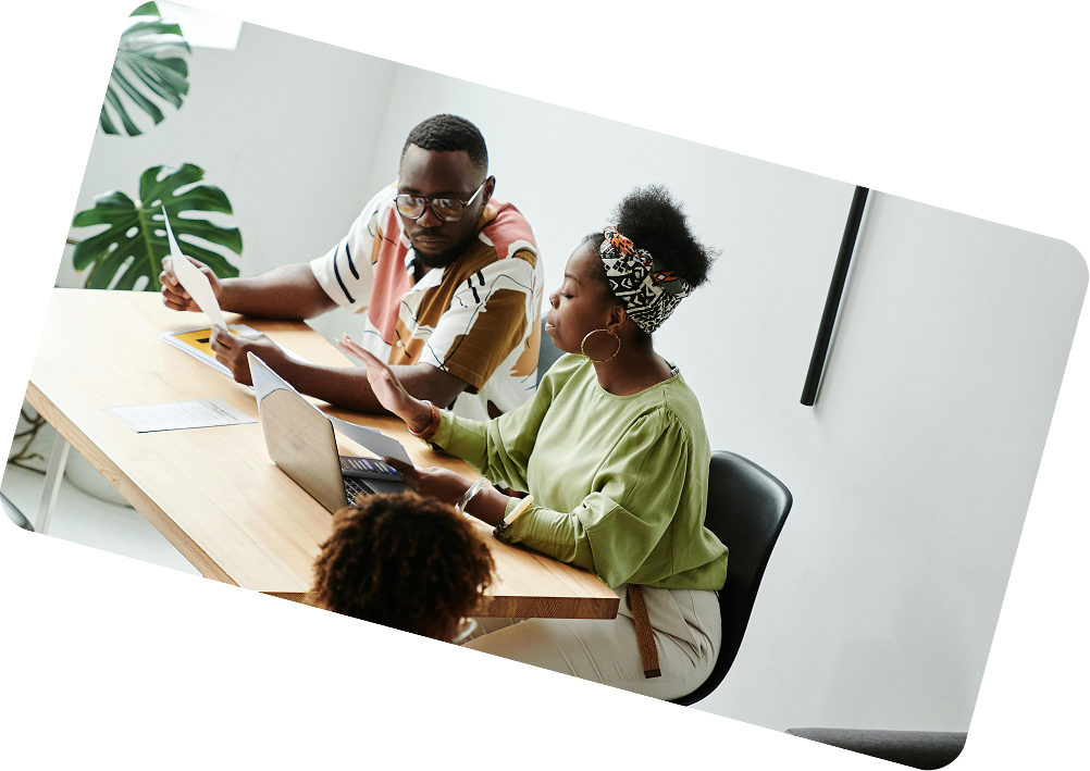 Two people sitting at a table reviewing documents and a laptop during a discussion.