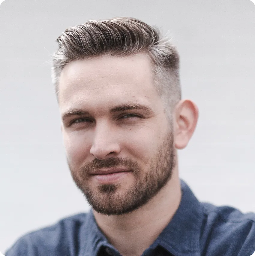 Portrait of a man with neatly styled short hair and beard wearing a blue shirt, looking into the camera.