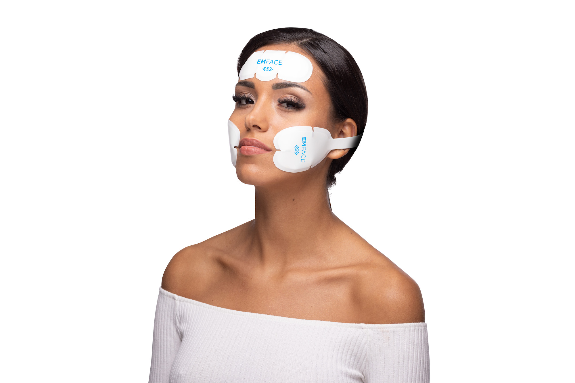 Woman wearing white EMFACE facial device pads on forehead and cheeks.
