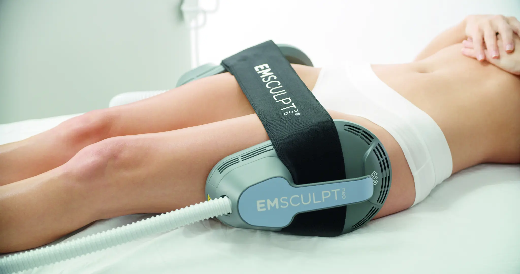 A woman laying on top of a bed with an emsculpt attached to her legs.