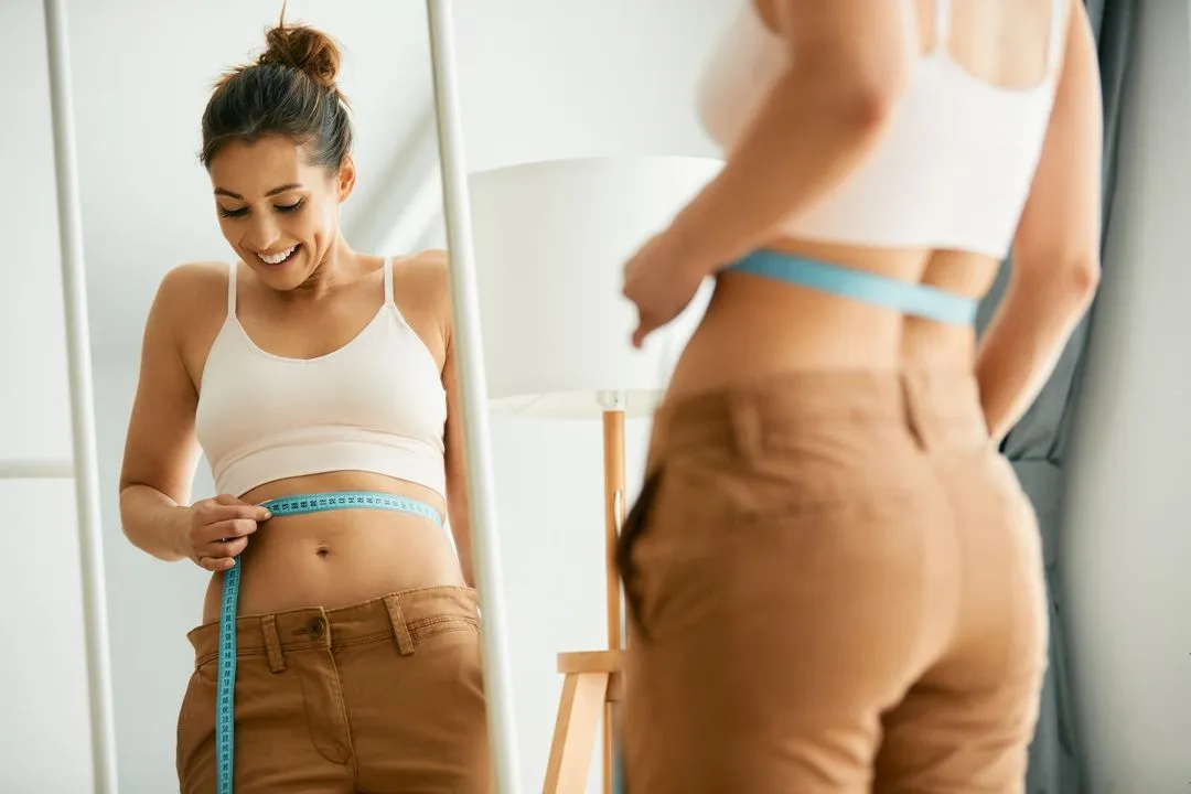 A woman measuring her waist with a tape.