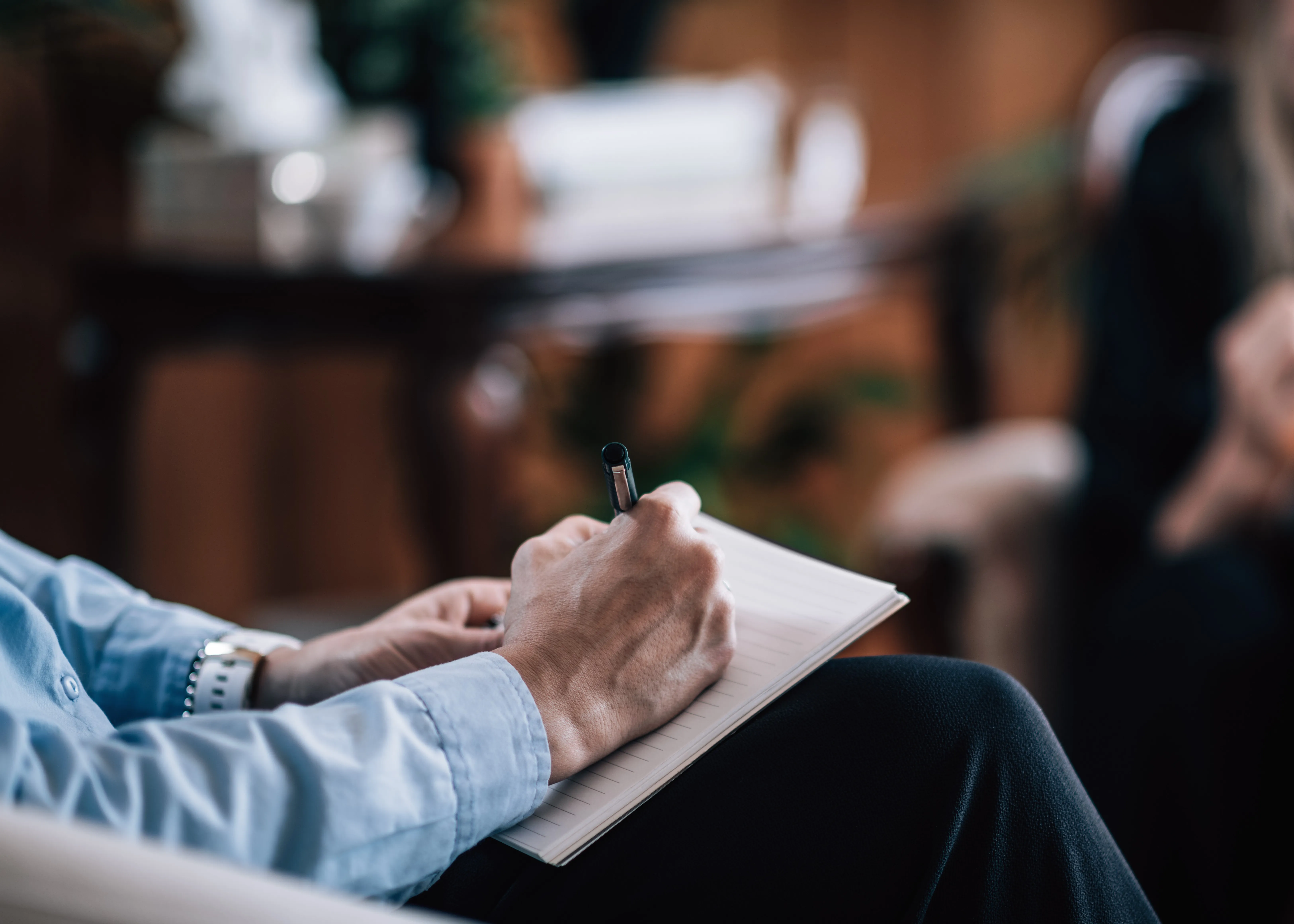 A person sitting in a chair writing on a notepad.