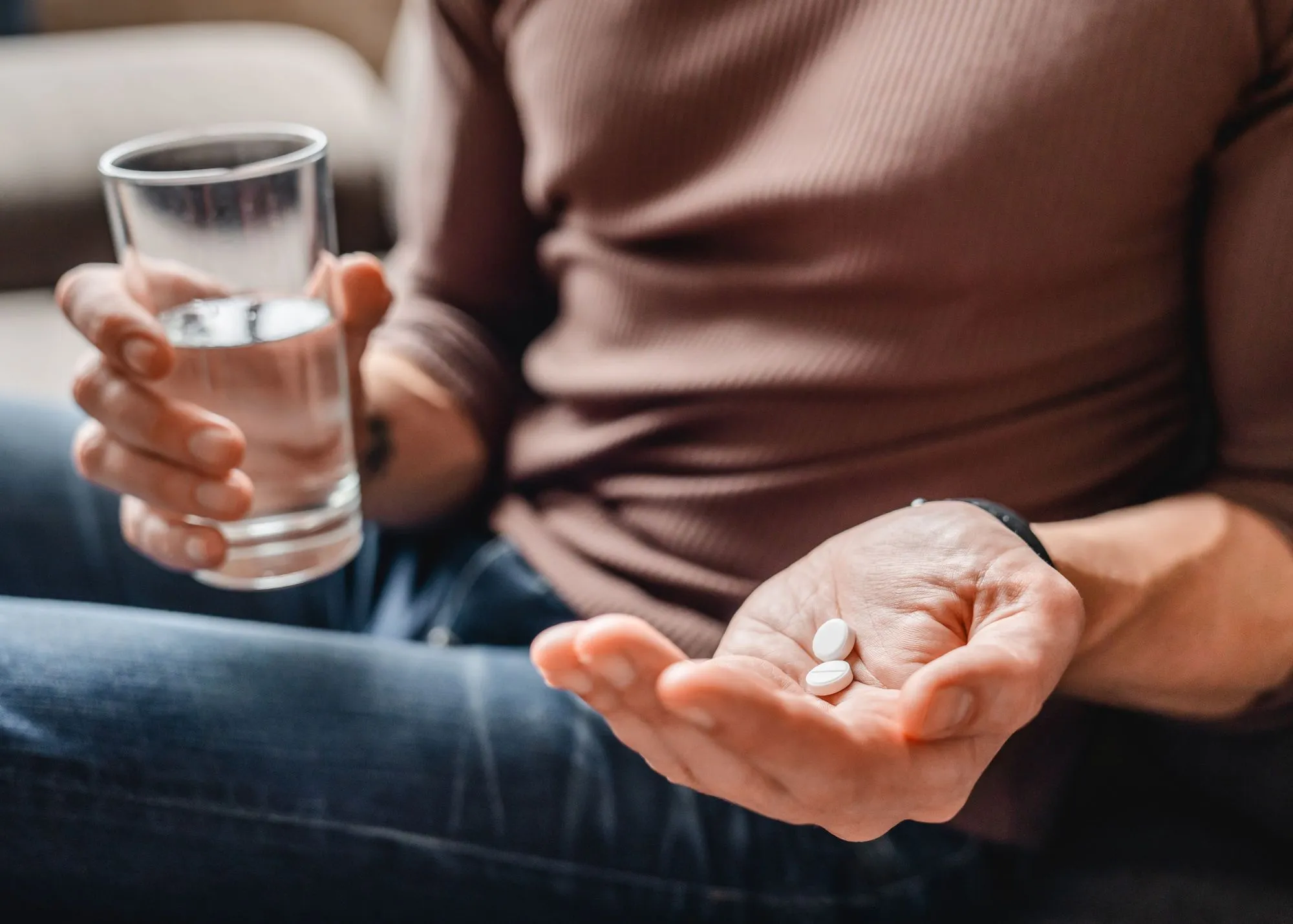 A man holding a glass of water and pills.