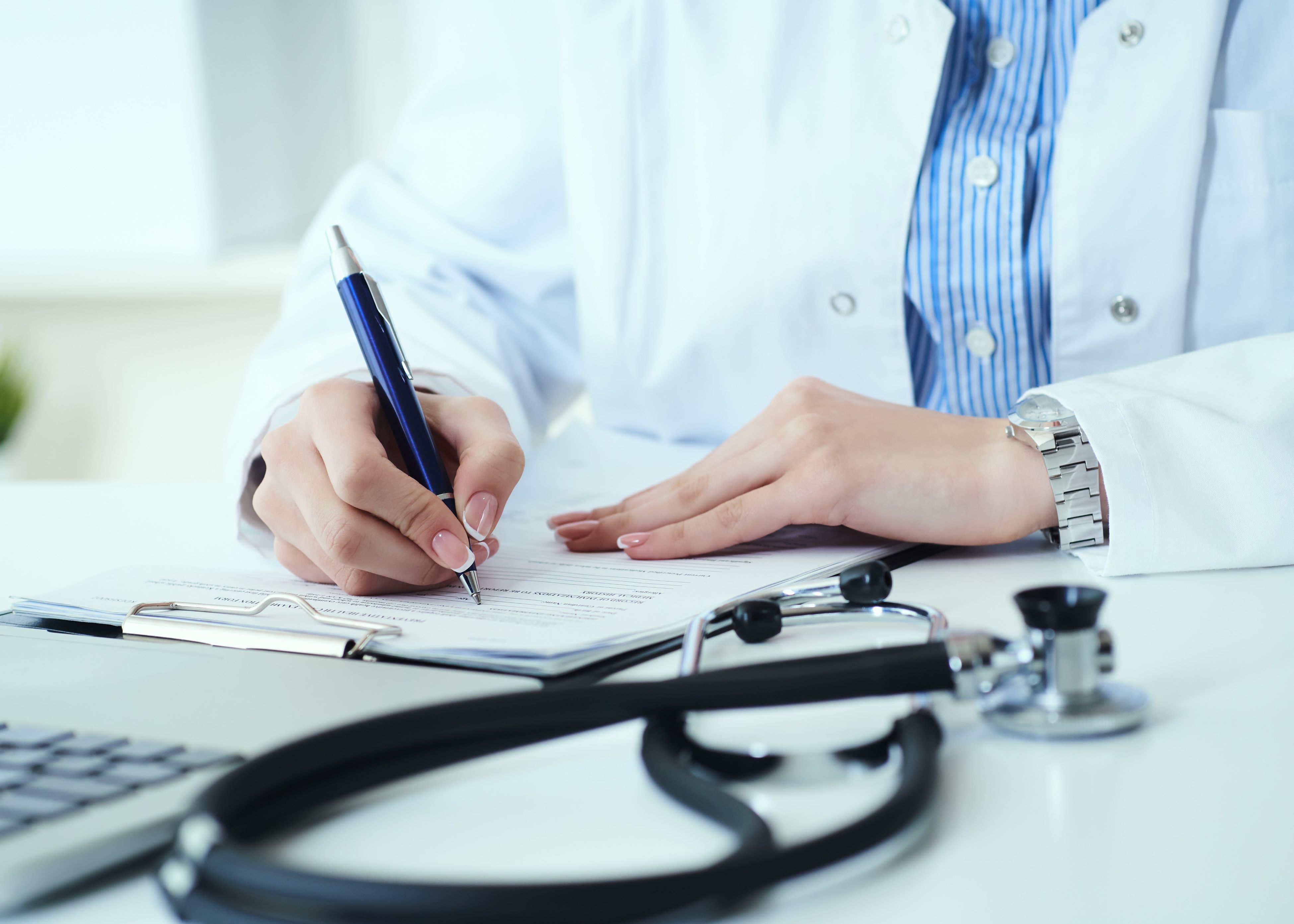 A doctor writing on a piece of paper with a stethoscope next to.