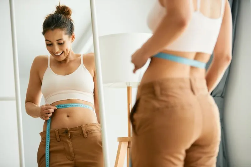 A woman measuring her waist with a tape.