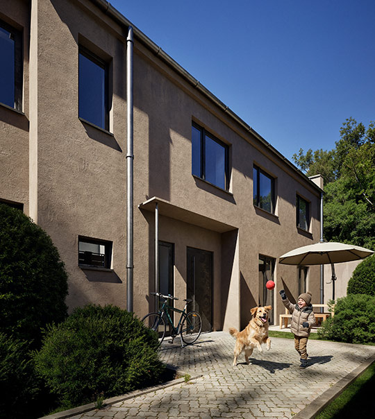 Smiling woman with shoulder-length brown hair sitting on a beige sofa while looking at her smartphone.