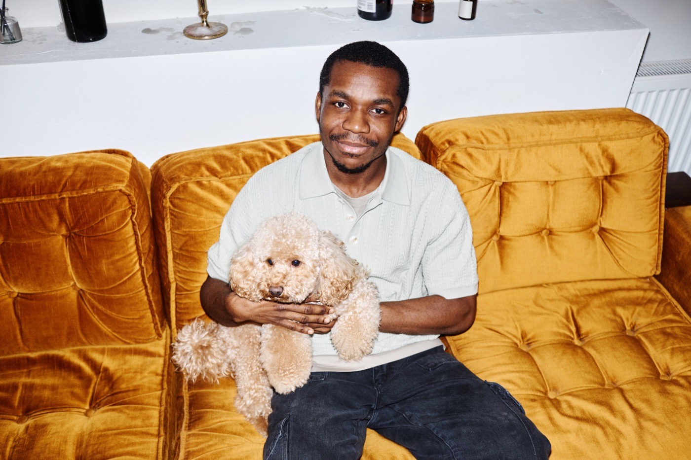 Man holding his poodle on a yellow couch at home