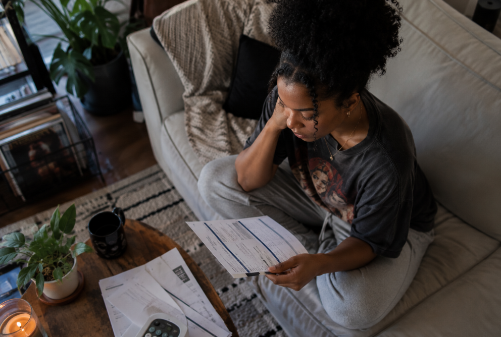 Renter sitting on a couch reviewing a paper bill in a softly lit living room.