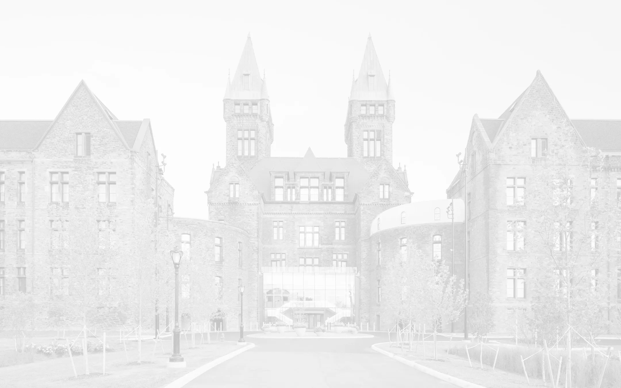 Richardson Olmsted Complex building with two central towers and modern glass entrance, surrounded by trees and lampposts.