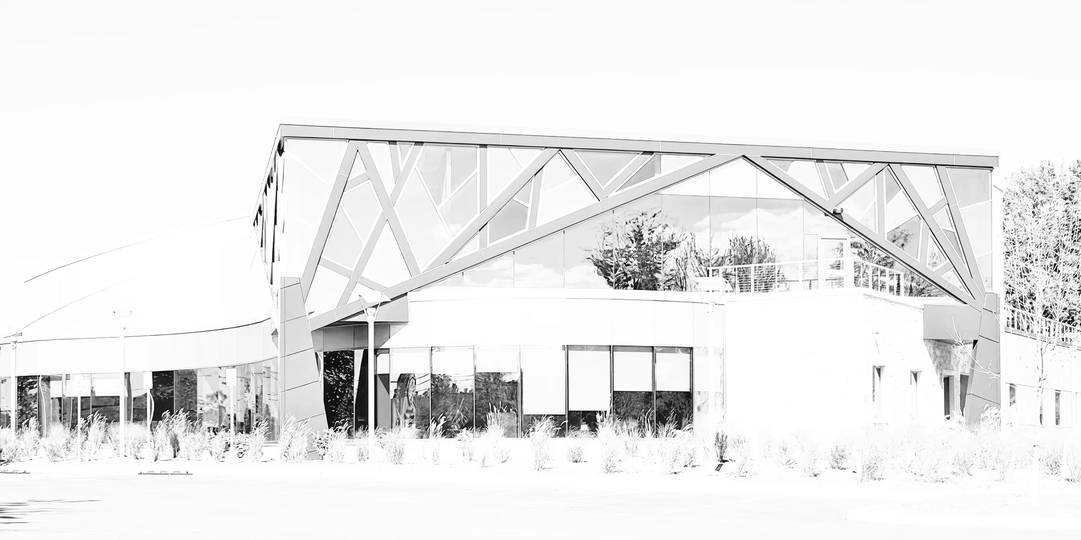 Modern curved building with large glass windows and diagonal metal framework reflecting trees.