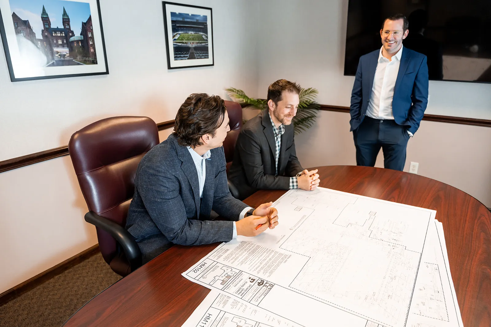 Three men in business attire discussing architectural blueprints on a conference table in an office.