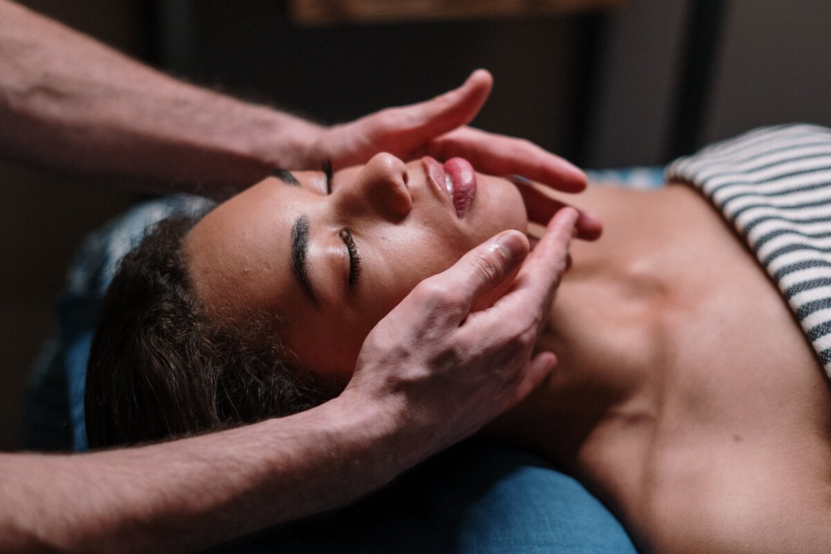 Woman with eyes closed receiving a facial massage with hands gently touching her face.
