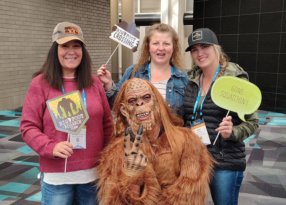 Caselle Sasquatch poses with conference attendees holding up a peace sign