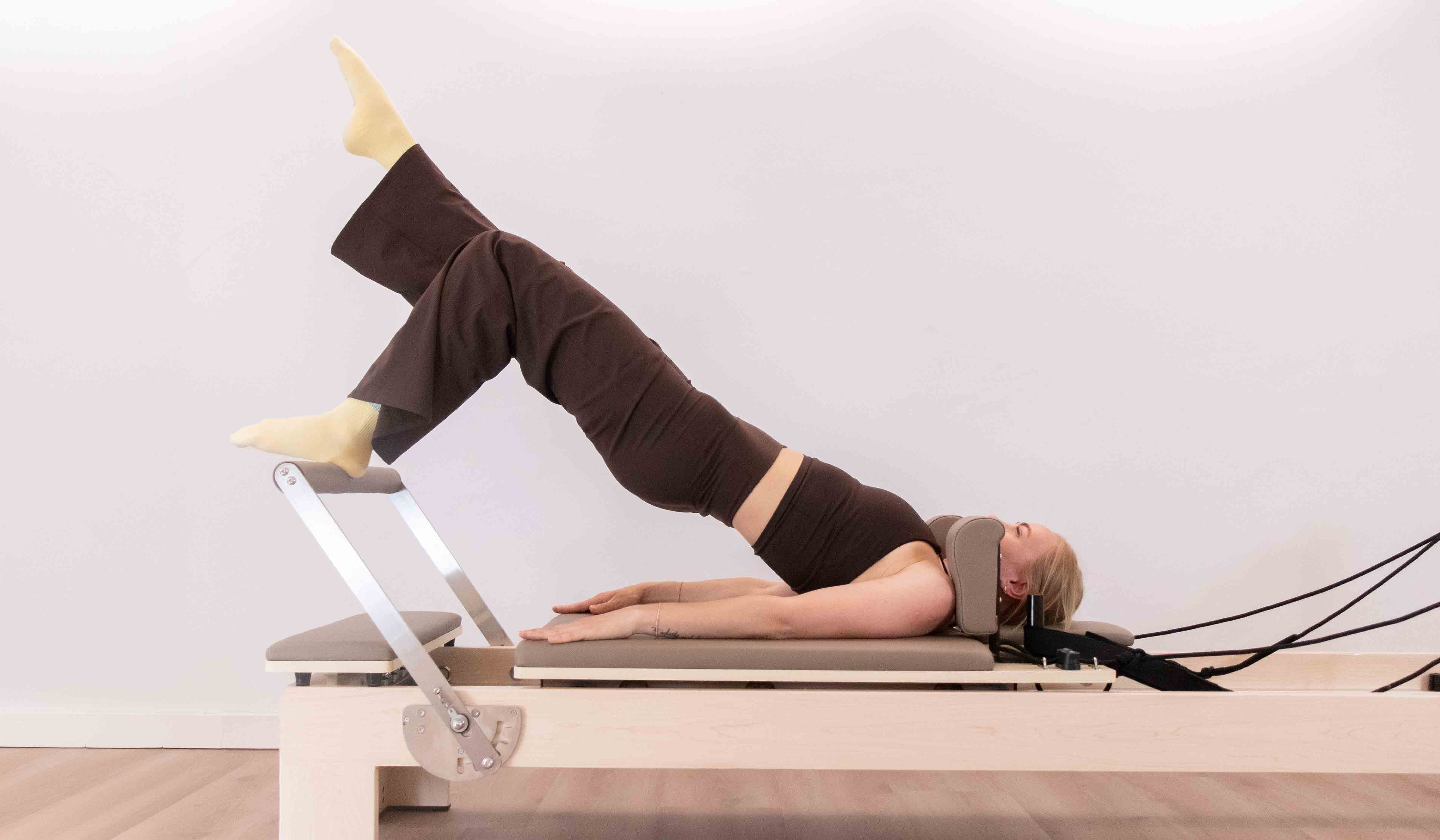 Woman doing Pilates exercise on reformer machine lifting hips with one leg raised.