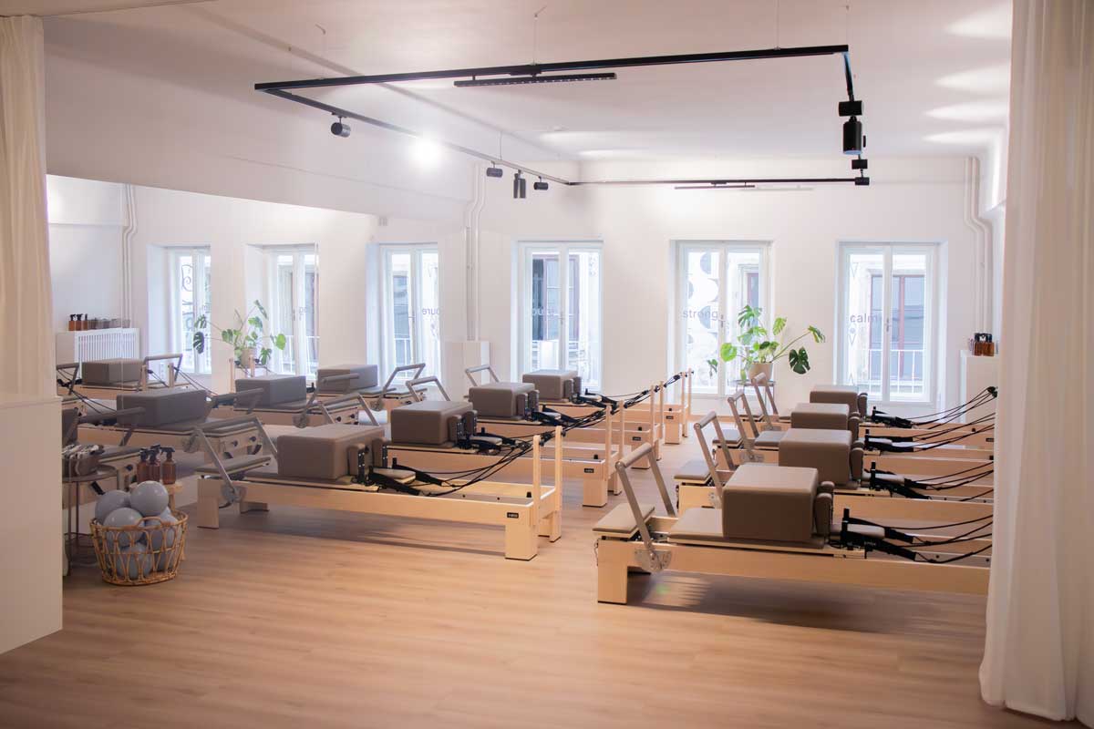 Bright Pilates studio with rows of reformer machines and large windows letting in natural light.