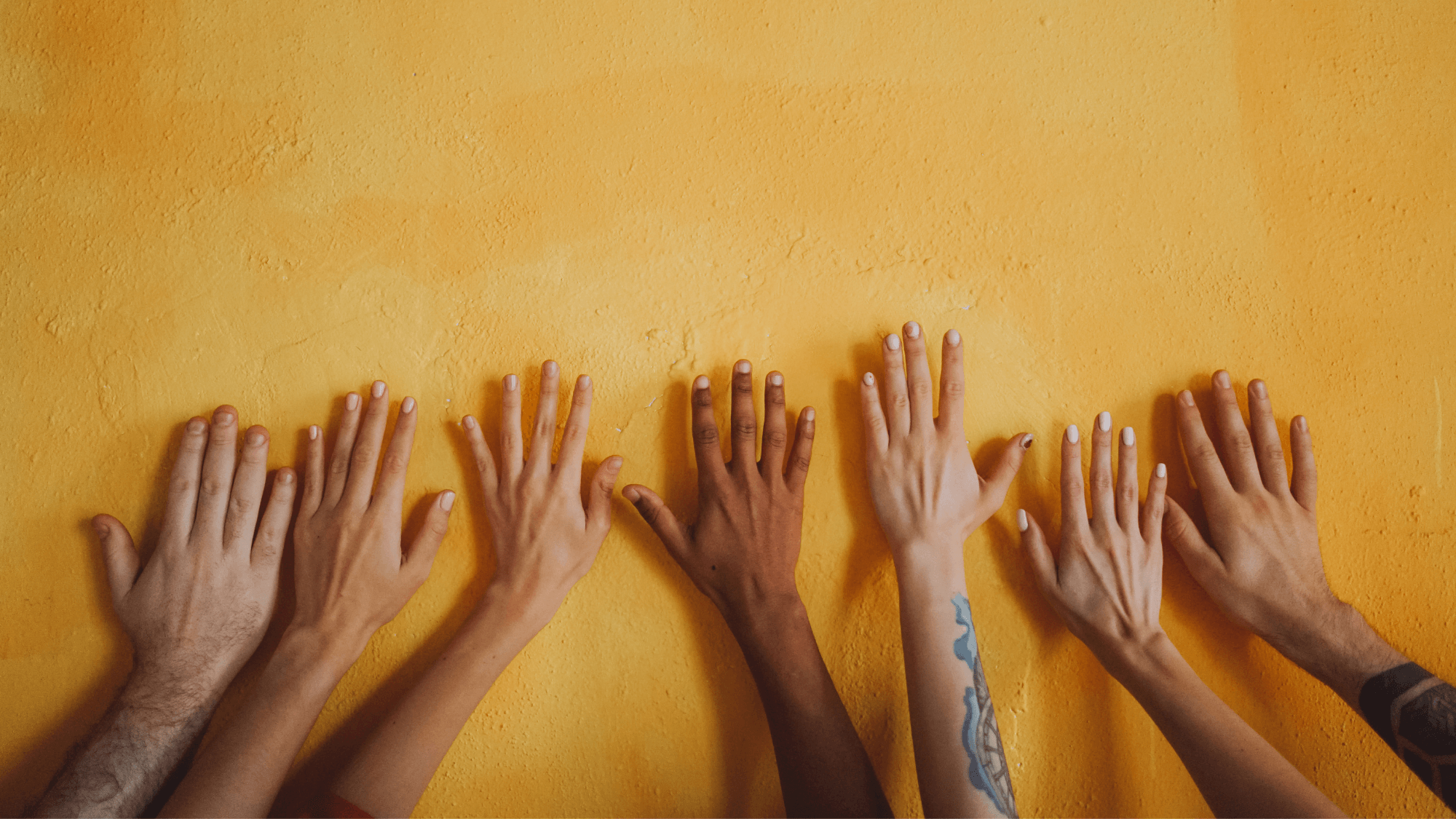 Different hands reaching out to a yellow-colored wall