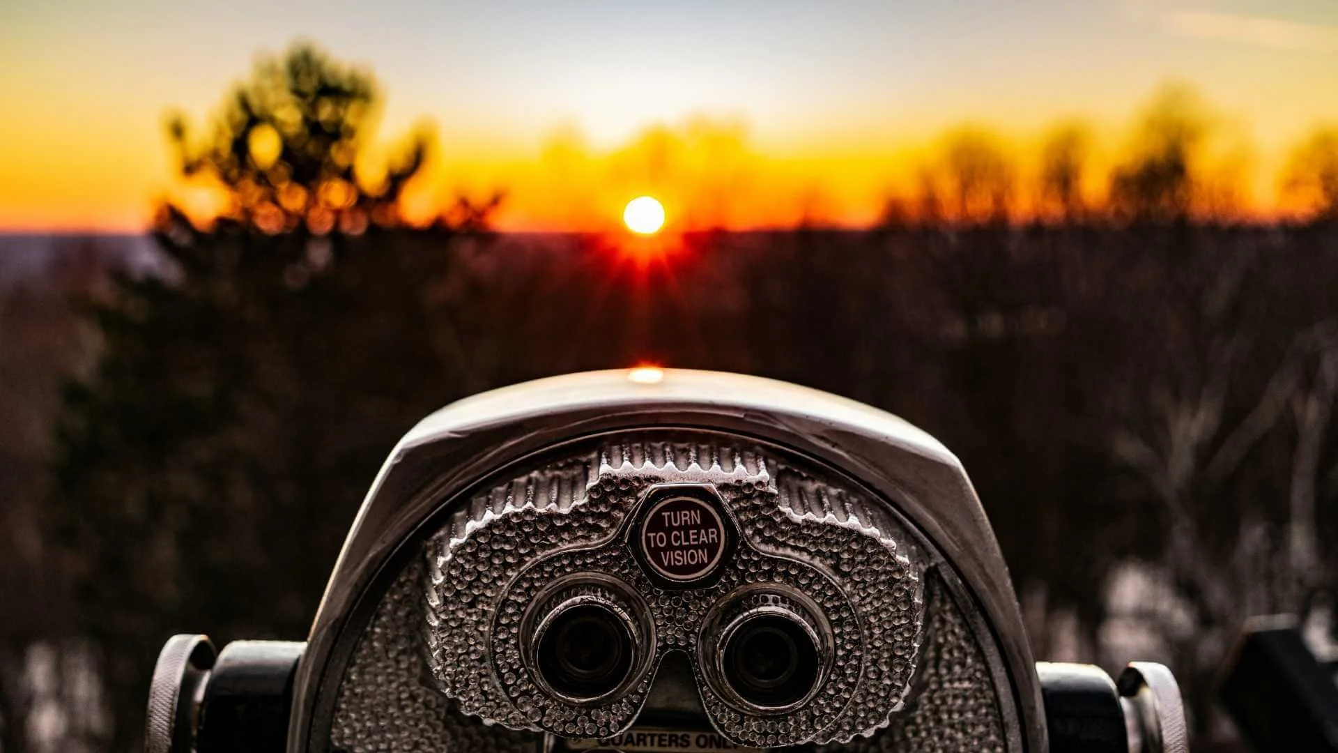 Steel binoculars with a text "Turn to clear vision" while pointing directly at the sunset