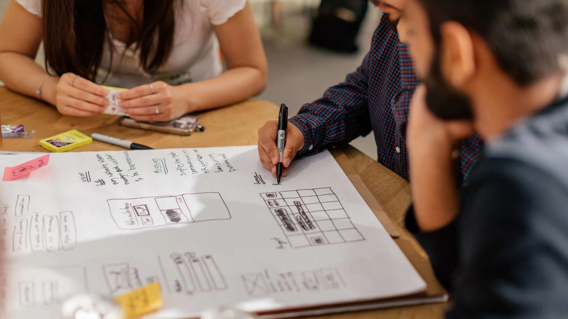 Three people working together while one is writing on a whiteboard using a marker