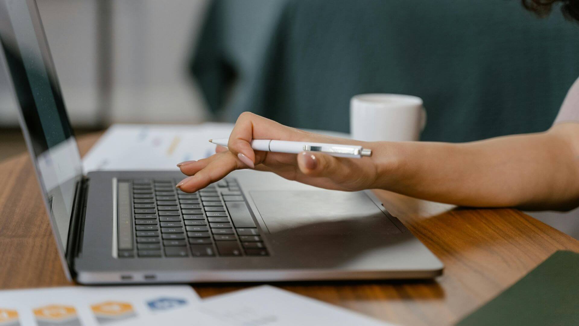 A woman holding a pen while typing on a laptop's keyboard