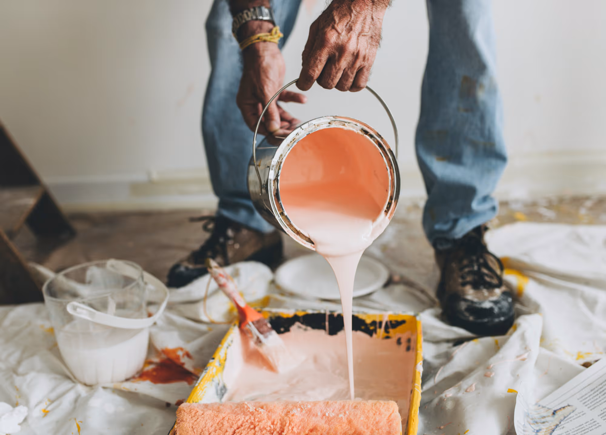 A man tipping pink paint into a painting tray as part of a renovation