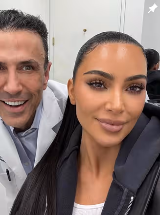 Close-up selfie of a smiling man in a white coat and a woman with long straight hair.