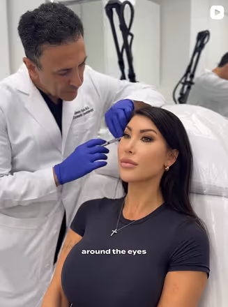 Medical professional wearing gloves performing a cosmetic procedure near a woman's eye in a clinical setting.