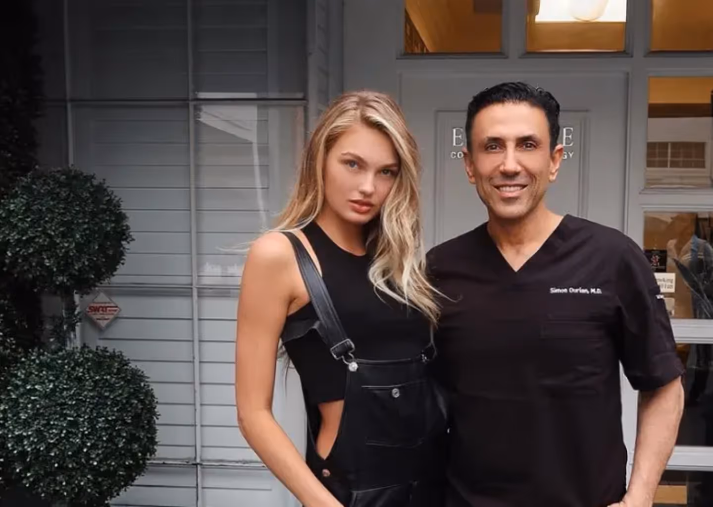 Smiling man in medical scrubs with name Simon Ourian, M.D. standing next to a woman with long blonde hair wearing a black sleeveless top and black overalls outside a building.
