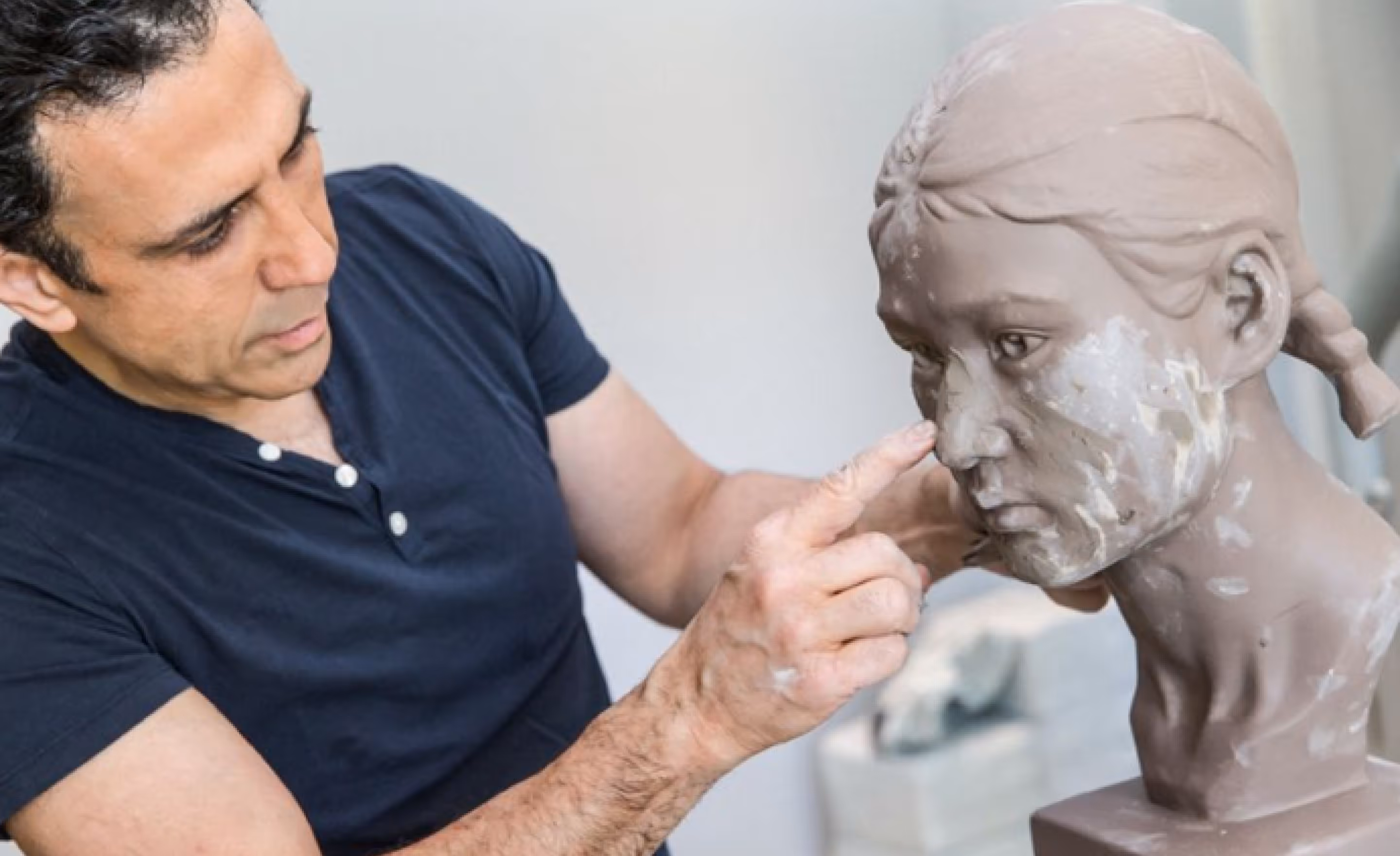 Sculptor shaping details on a clay bust of a woman with braided hair.