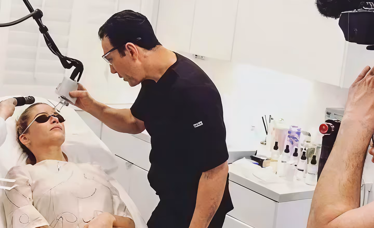 A medical professional wearing protective glasses performing a laser treatment on a woman lying down with protective eyewear.