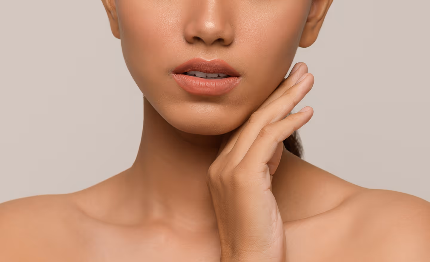 Close-up of a woman touching her cheek with her hand, showing smooth skin and natural lips.