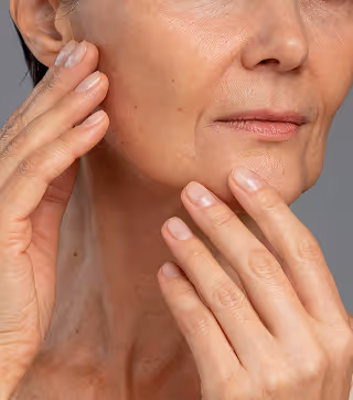 Close-up of a mature woman's lower face and hands gently touching her cheek and chin.