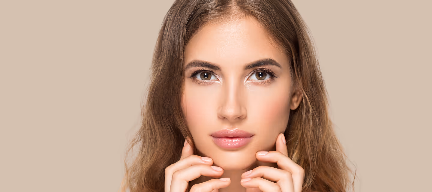 Close-up of a young woman with clear skin and glossy lips gently touching her face.