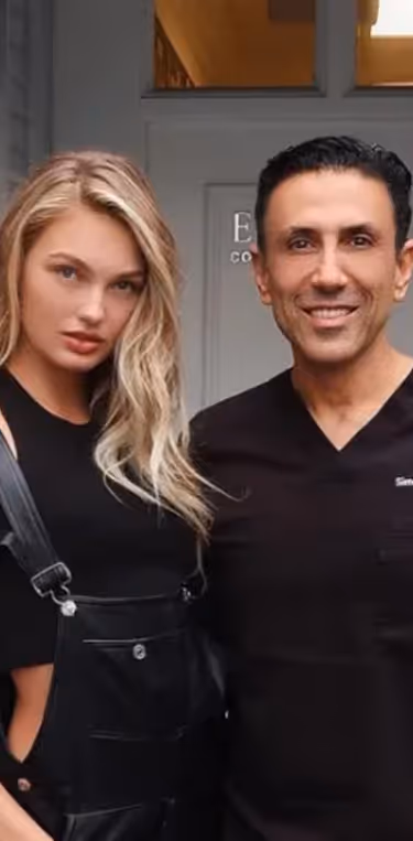 Smiling man in black scrubs standing next to a woman with long blonde hair wearing a black top and black overalls.