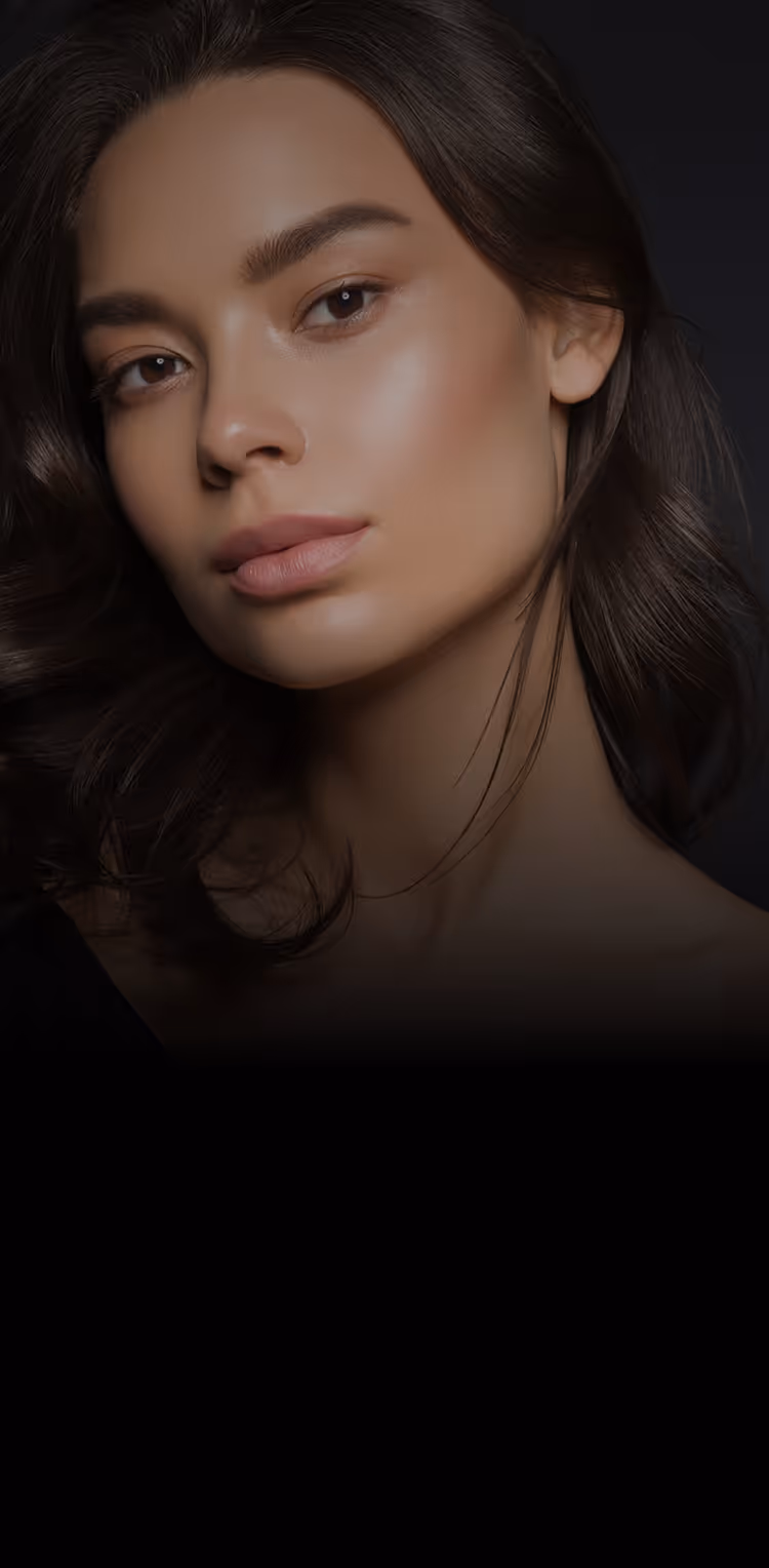 Close-up portrait of a woman with smooth skin, dark hair, and natural makeup against a black background.