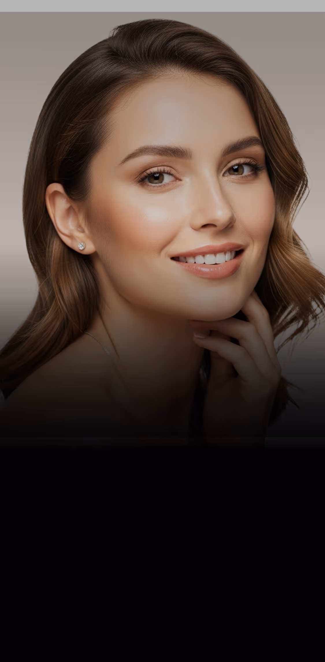 Smiling woman with clear skin holding her face with both hands against a gray background.