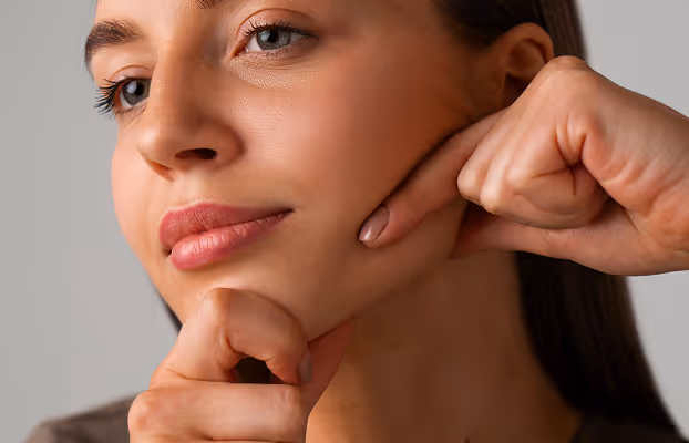 Close-up of a woman pressing her fingers against her jaw and chin with a slight smile.