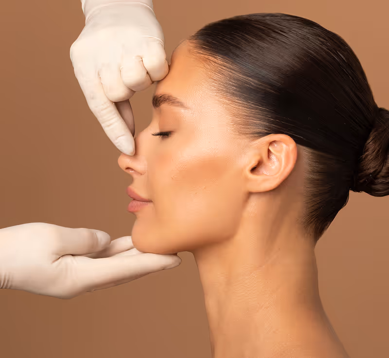 Profile of a woman with eyes closed, face gently held by gloved hands, suggesting a cosmetic checkup.