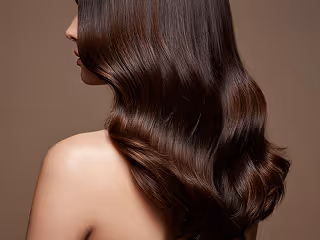 Woman with long, shiny, wavy brown hair seen from behind and side profile on brown background.