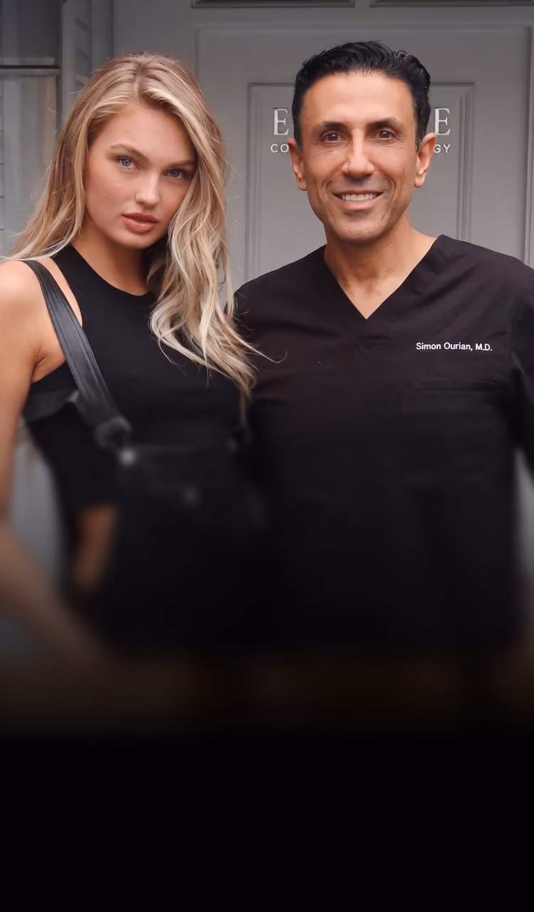 Smiling man in medical scrubs and woman with blonde hair pose together indoors.