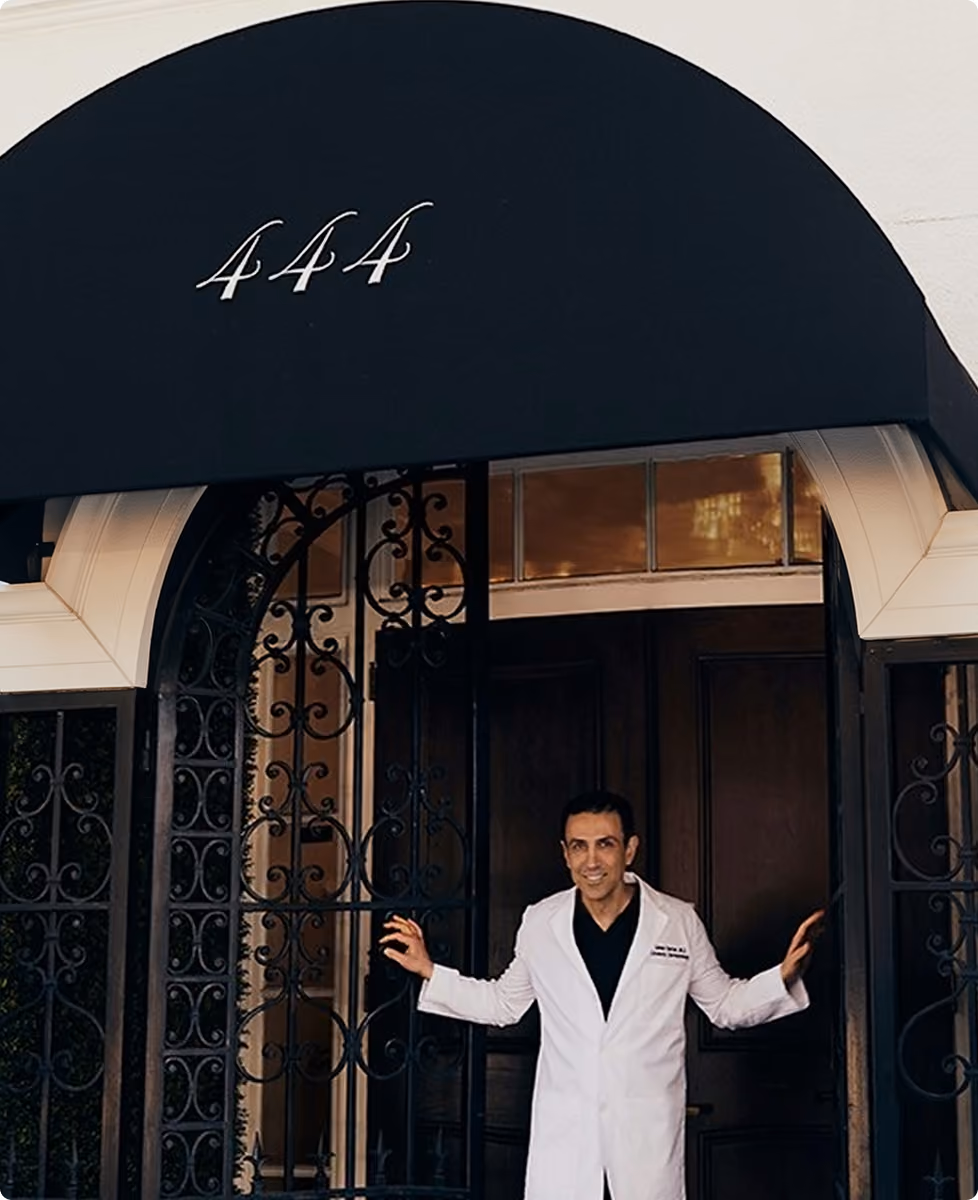 Man in white coat opening black wrought-iron gates at entrance numbered 444 with Epione sign.