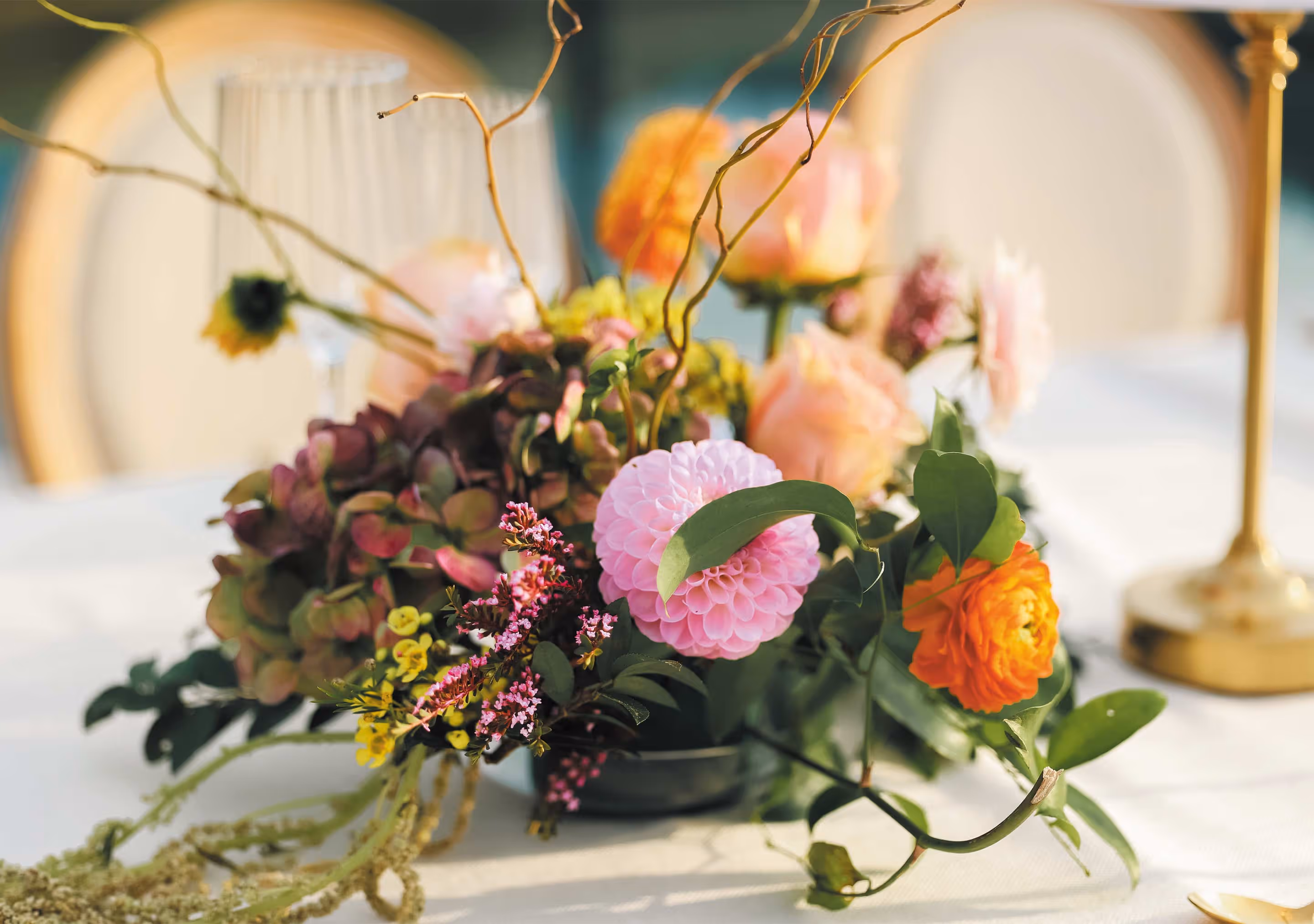 Colorful floral centerpiece with pink, orange, and yellow flowers and green leaves on a white tablecloth.