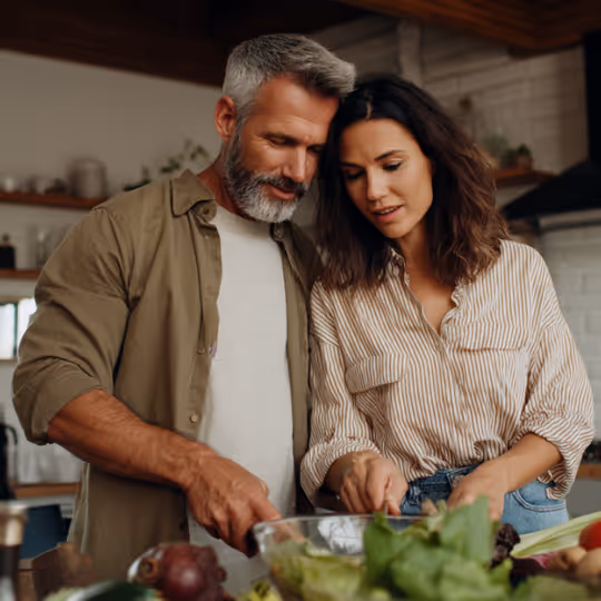 Couple cooking together in a kitchen, chopping vegetables on a counter.