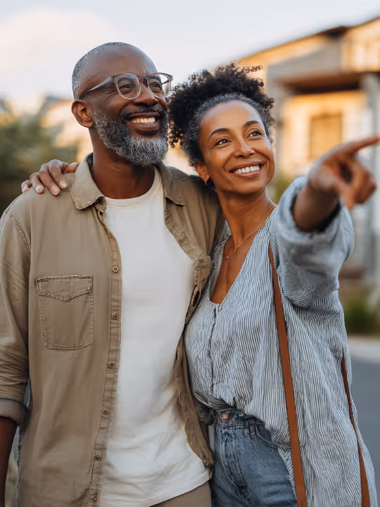 Smiling couple outdoors with the woman pointing at something in the distance.