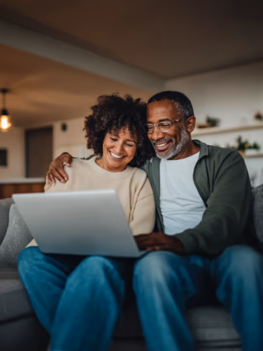 Smiling couple sitting on a couch looking at a laptop together in a cozy living room.