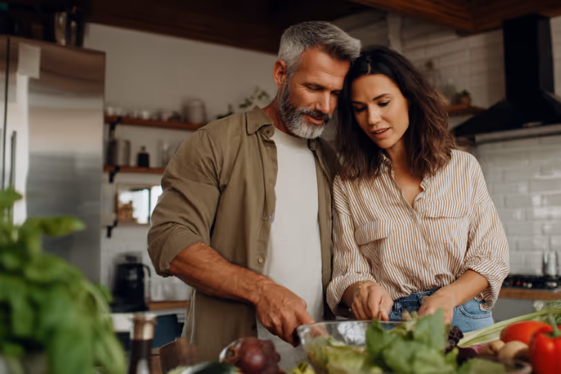 Couple preparing a salad together in a modern kitchen with fresh vegetables on the counter.