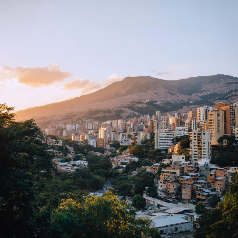 Cityscape with tall buildings against a mountain backdrop at sunset.