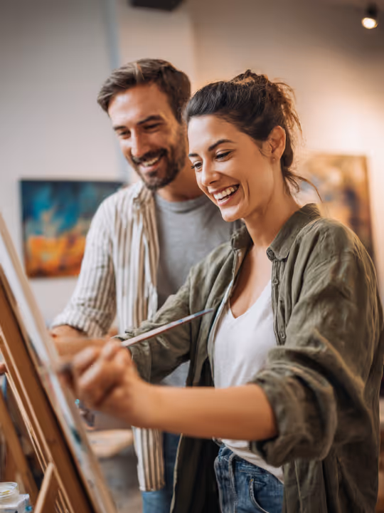 Smiling couple painting together on an easel in an art studio.